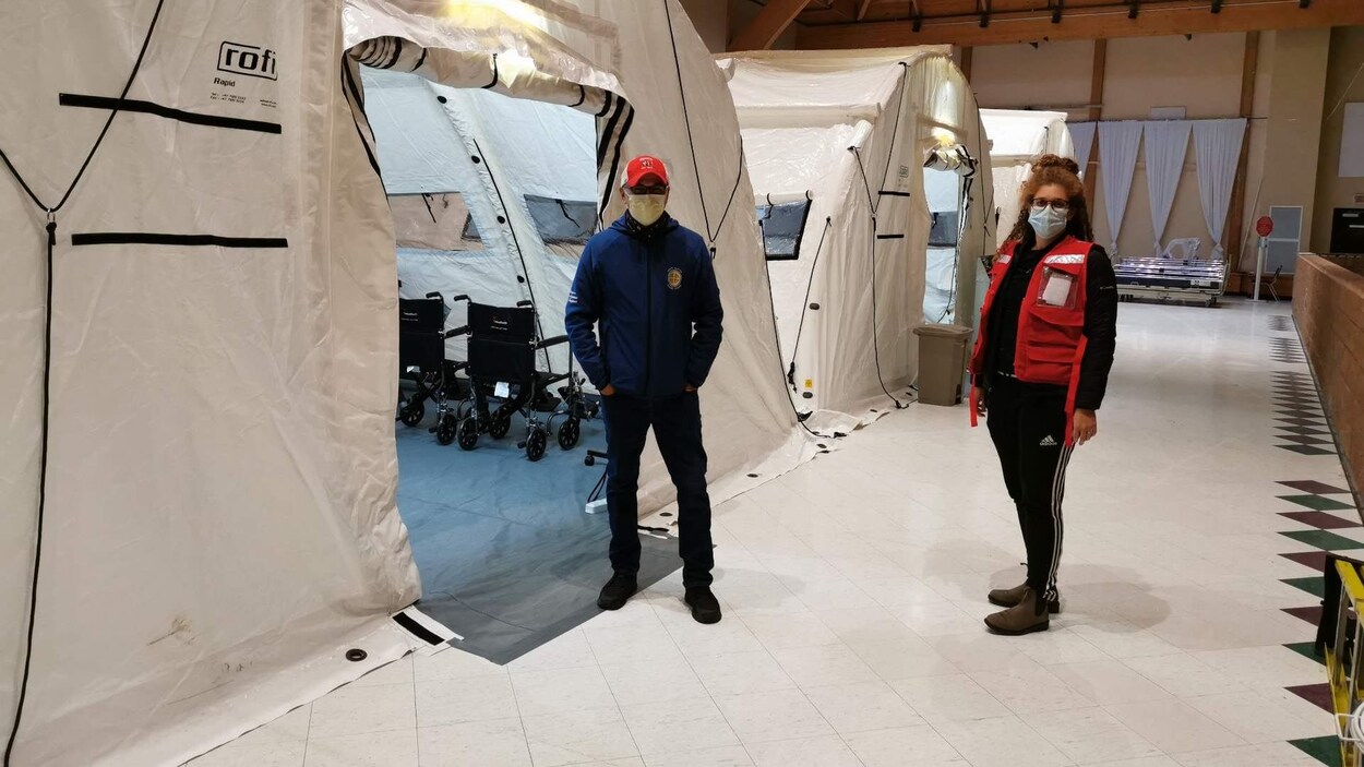 Deux personnes prennent la pose devant des tentes médicales installées dans une salle de banquet de Chisasibi.