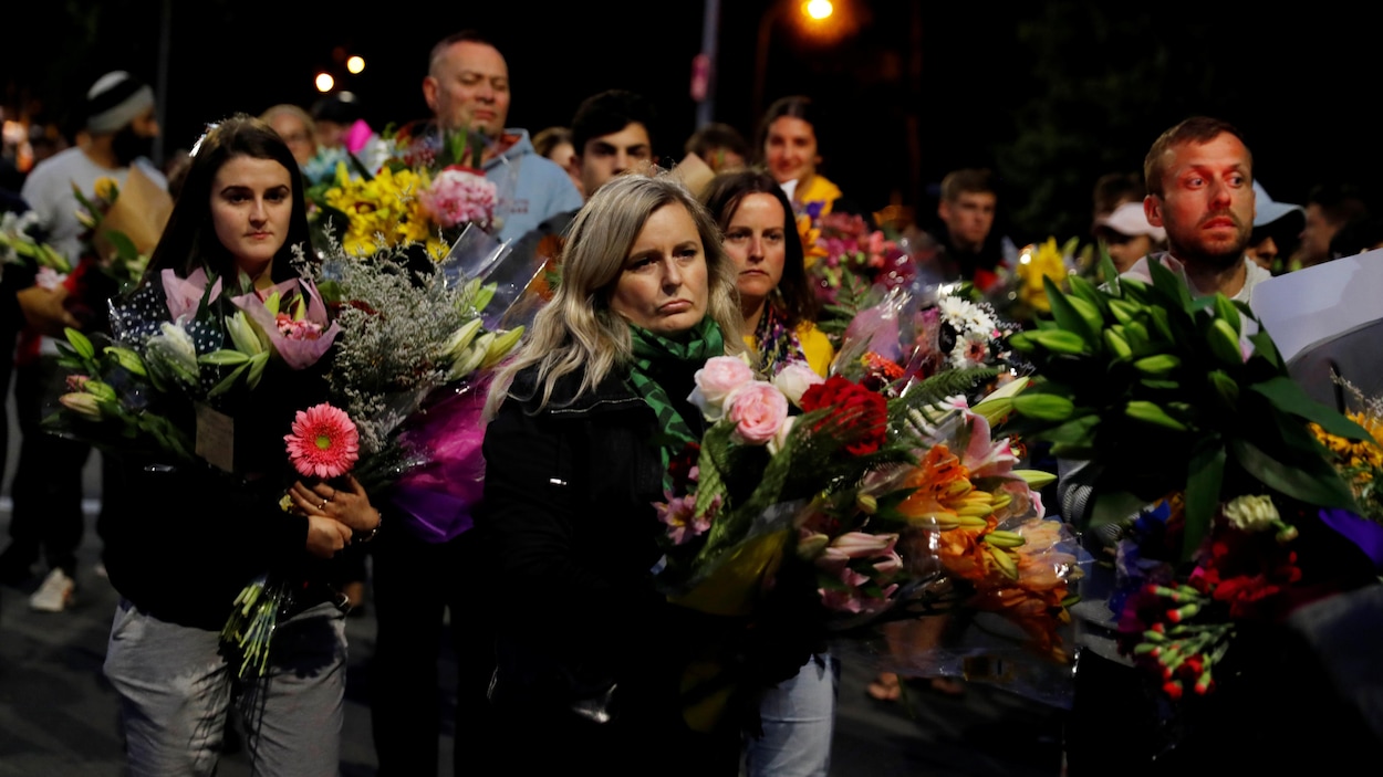 Des dizaines de personnes marchent avec des bouquets de fleurs dans les mains.