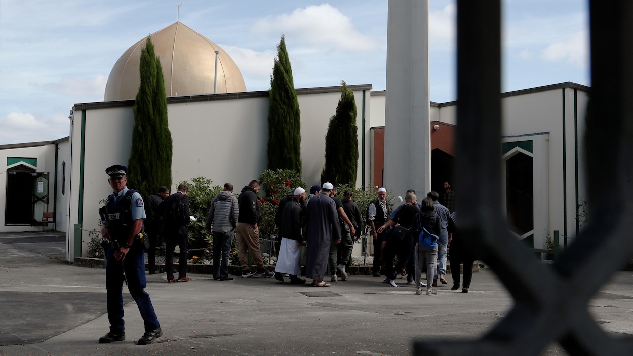 Un policier armé devant quelques fidèles à l'extérieur d'une mosquée