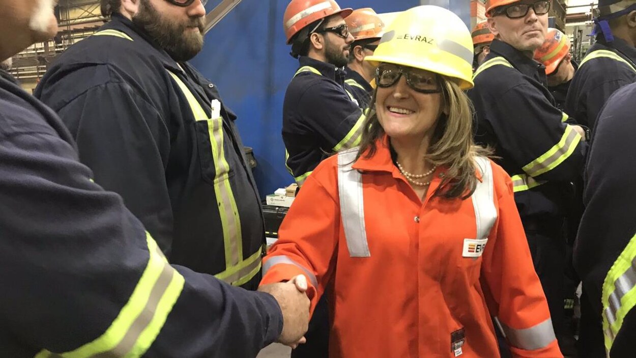 Une femme en uniforme de travail serre la main d'un homme devant un groupe de travailleurs