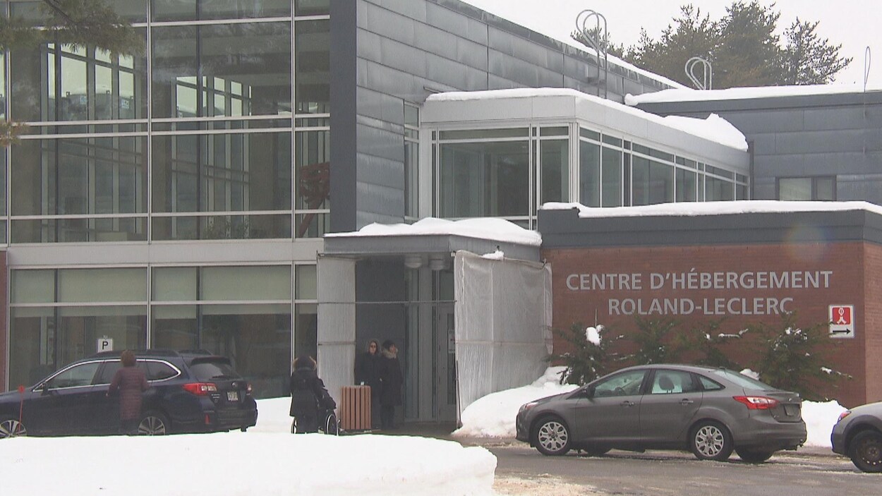 Un édifice avec l'inscription «Centre d'hébergement Roland-Leclerc» affichée sur son mur extérieur. En hiver. Des automobiles sont stationnées devant.