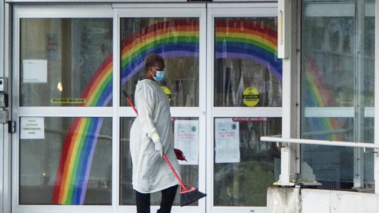 Une employée masquée passe le balai devant la porte d'entrée du CHSLD.