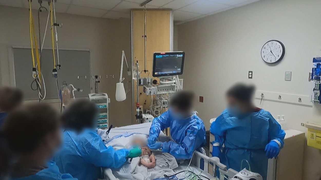 Cinq personnes donnent des soins à un bébé dans une salle d'hôpital.