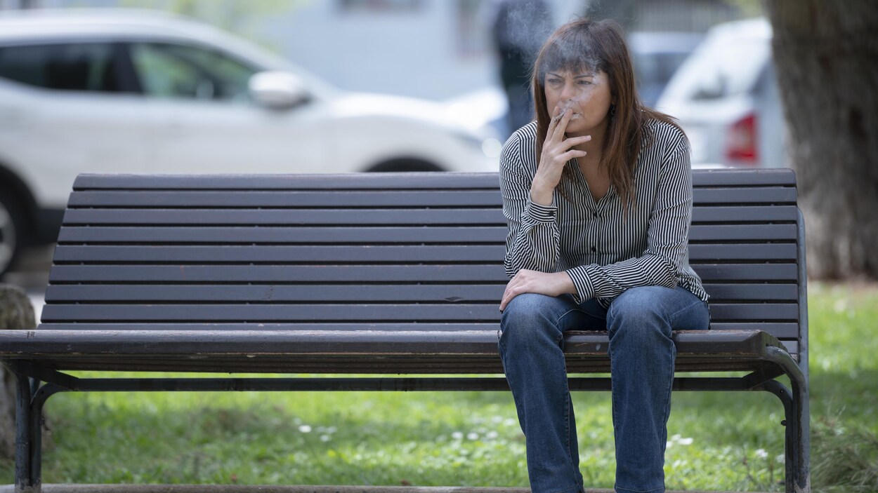Femme assise sur un banc public, fumant une cigarette.
