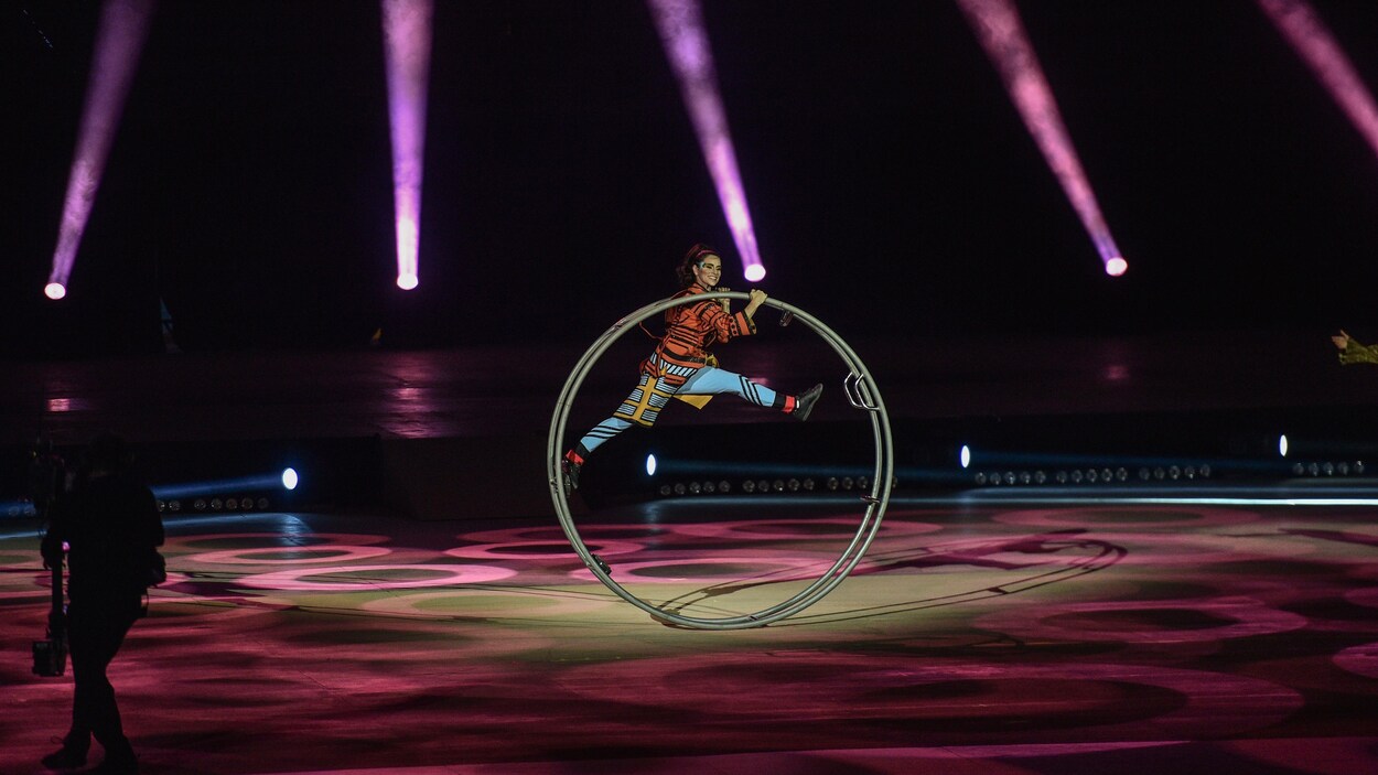 Une artiste du Cirque du Soleil traverse la scène en faisant avancer une grande roue.