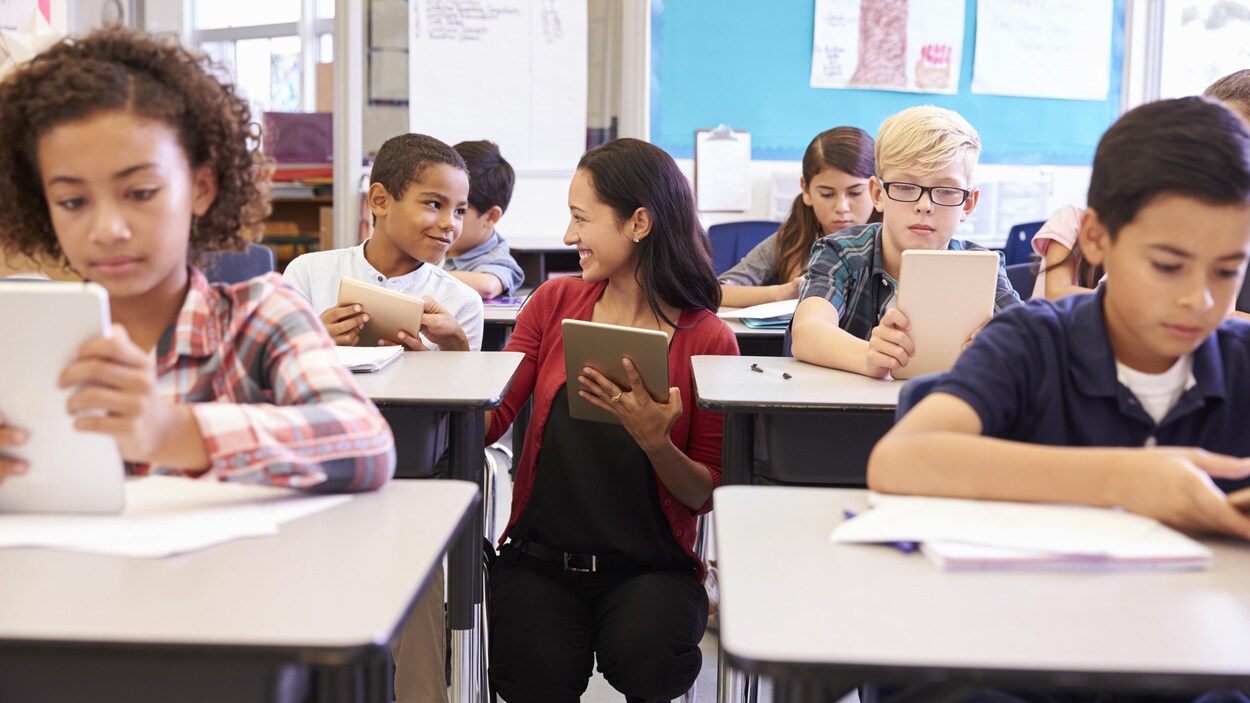 Des élèves d'âge primaire dans une classe, tous équipés d'une tablette électronique. Des élèves d'âge primaire dans une classe, tous équipés d'une tablette électronique.