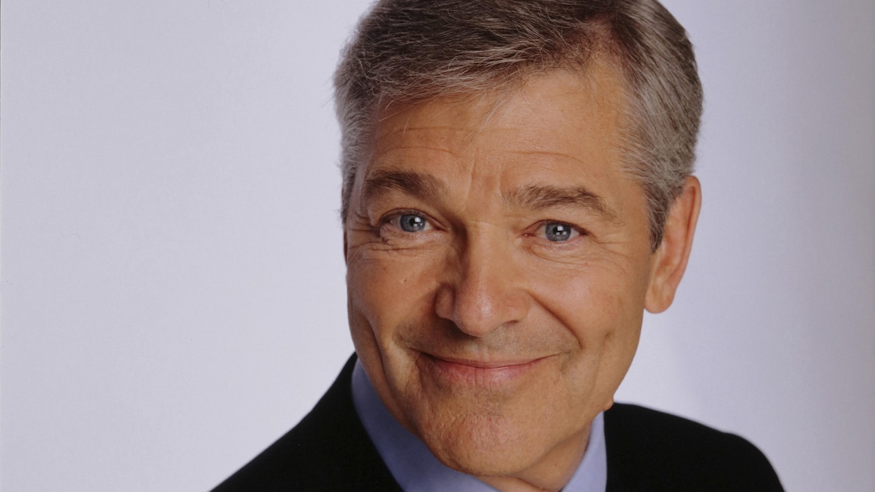 Claude Beauchamp souriant devant un fond bleu.