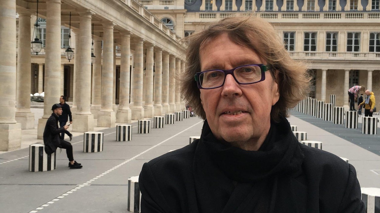 Le poète regarde dans l'objectif de l'appareil photo, les bras croisés, dans la cour intérieure du Palais-Royal, à Paris.
