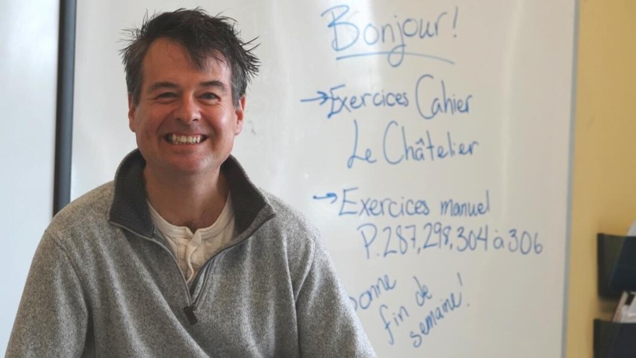 Claude Vallée dans sa classe assis sur son bureau.