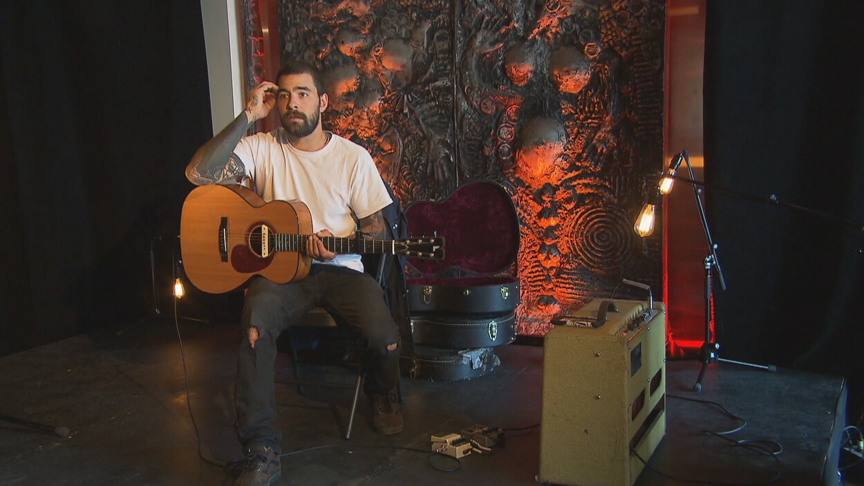 Clement Jacques est assis ave sa guitare sur les genoux.