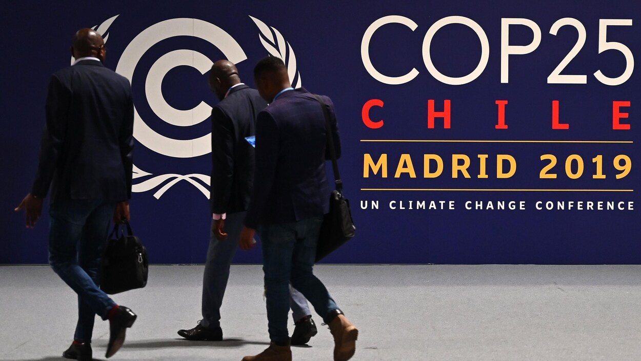 Des hommes entrent devant un panneau qui indique le site de la COP25 à Madrid.