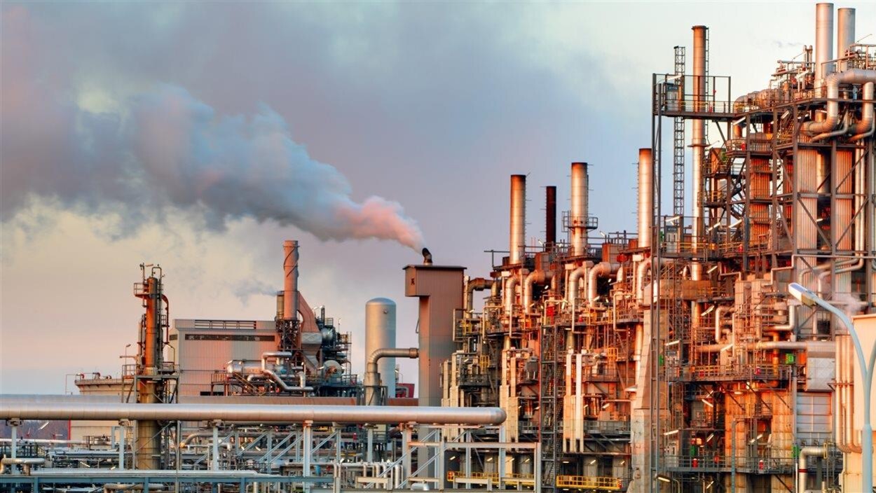 Une usine pétrochimique fume au coucher du soleil.
