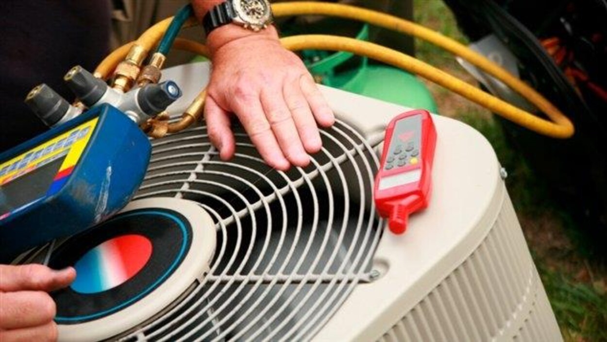 Une main est posée sur une thermopompe sur laquelle sont posés des appareils de mesure.