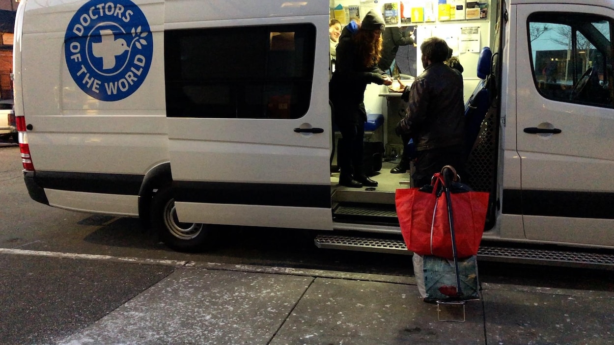 Un homme se tient devant la porte du véhicule de Médecins du Monde et se fait donner quelque chose par l'infirmière