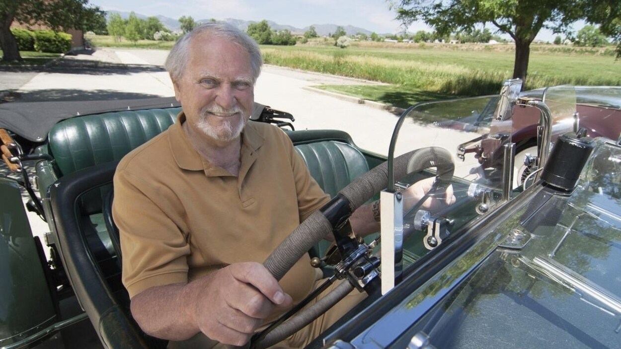 Clive Cussler, au volant d'une voiture, porte une barbe blanche.