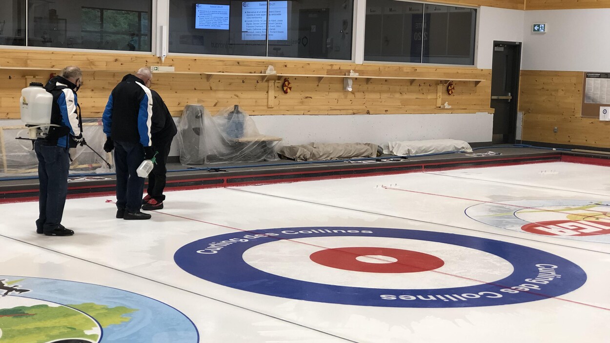 Trois hommes arrosent une glace de curling.