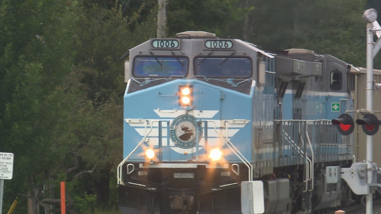 Une locomotive bleue avec des lumières allumées en avant passe sur une traverse ferroviaire.