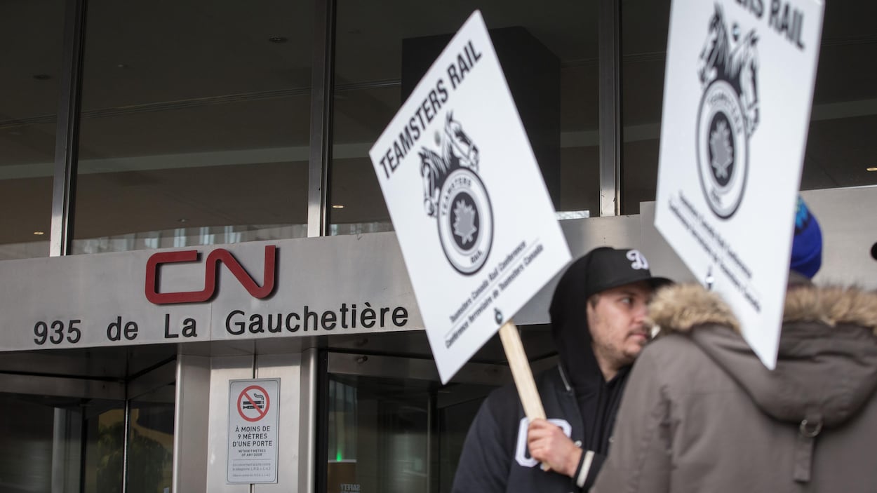 Deux personnes tiennent des pancartes du syndicat des Teamsters devant les bureaux du CN.