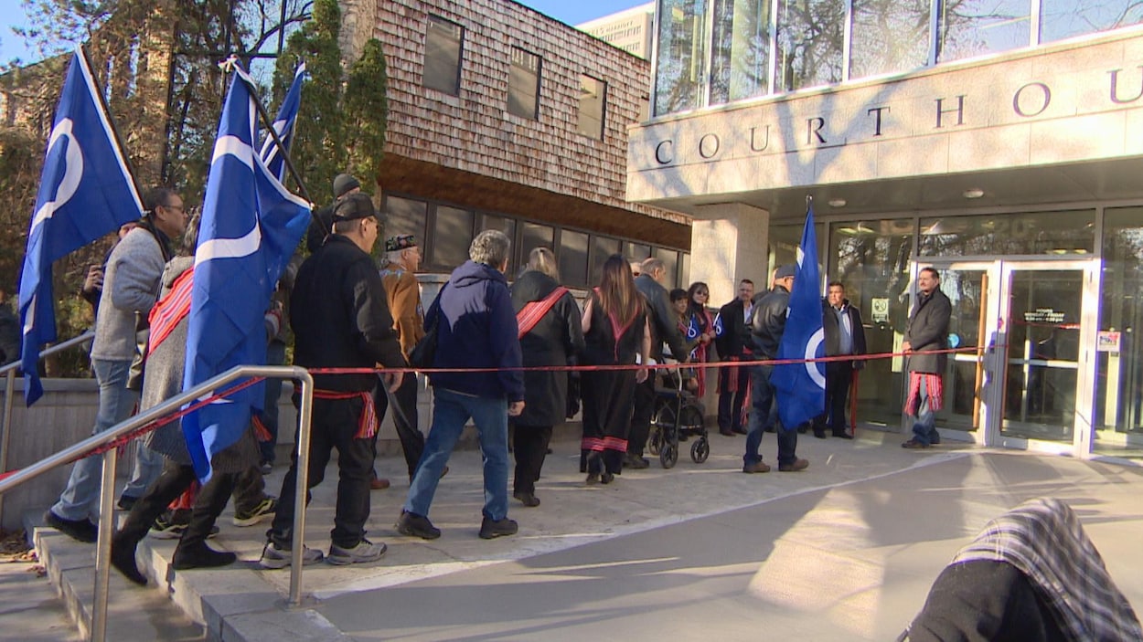 Des Métis entrent dans l'édifice de la Cour fédérale. Certains portent de larges drapeaux métis.