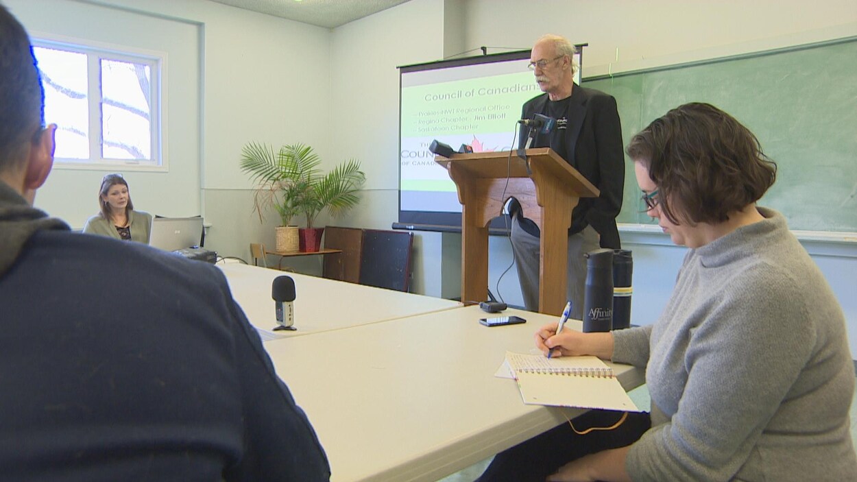 Un homme devant un lutrin parle à des gens qui prennent des notes.