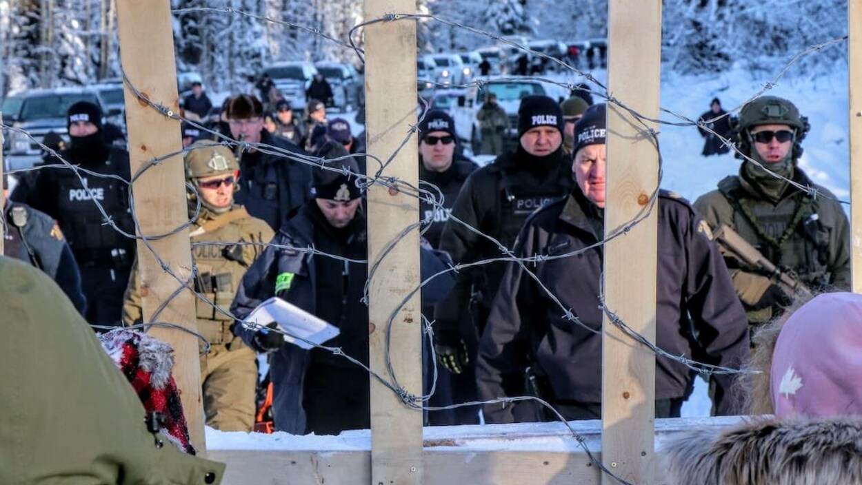 Des agents de la GRC négocient avec des membres des Premières Nations derrière un fil barbelé.