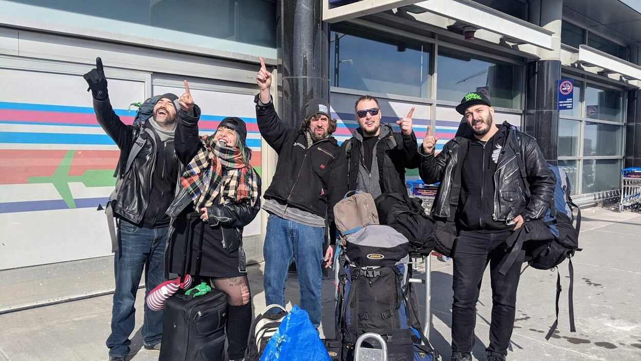 Les quatre musiciens et la directrice de tournée pointent le ciel, entourés de leur bagages.