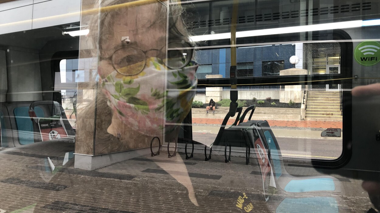 Réflexion d'une femme masquée dans une vitre d'autobus.
