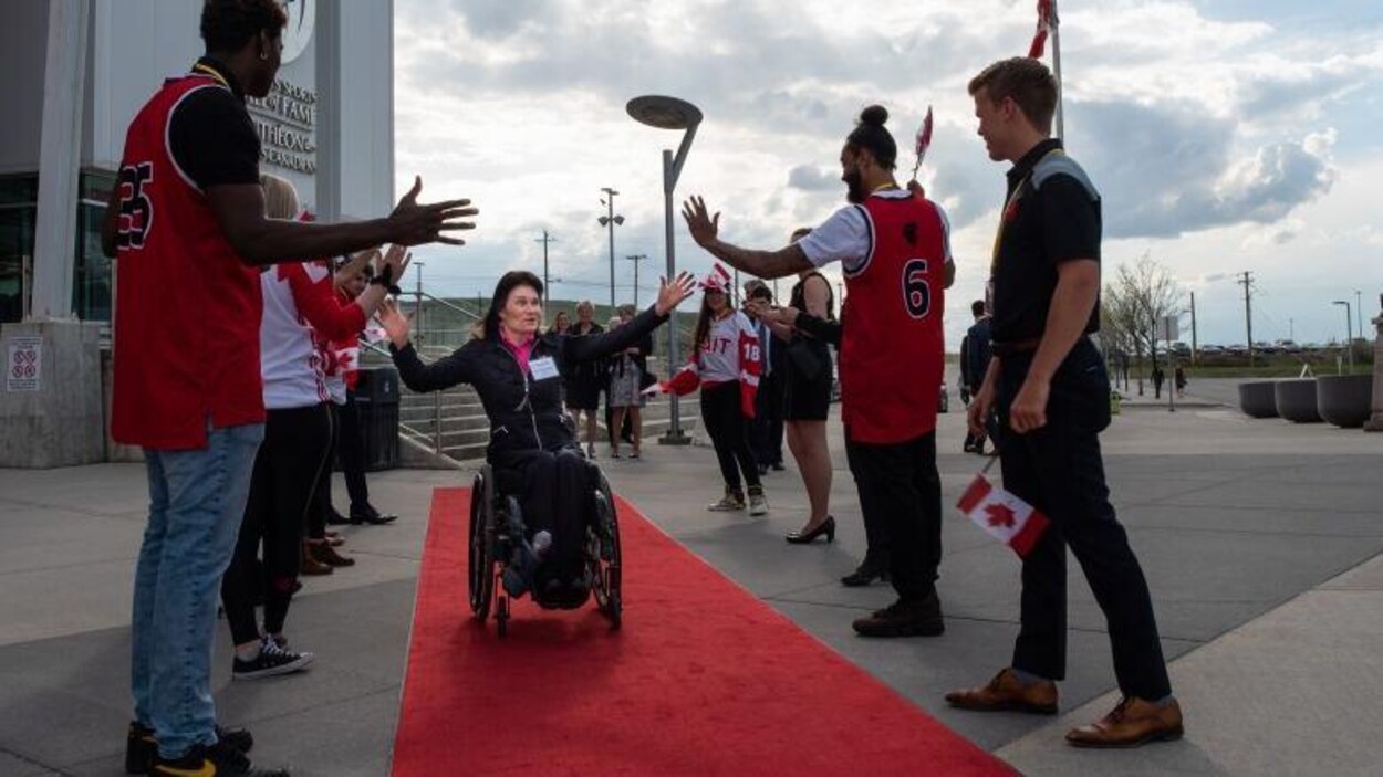 Colette Bourgonje avance sur un tapis rouge en fauteuil roulant pendant que des supporteurs la saluent.