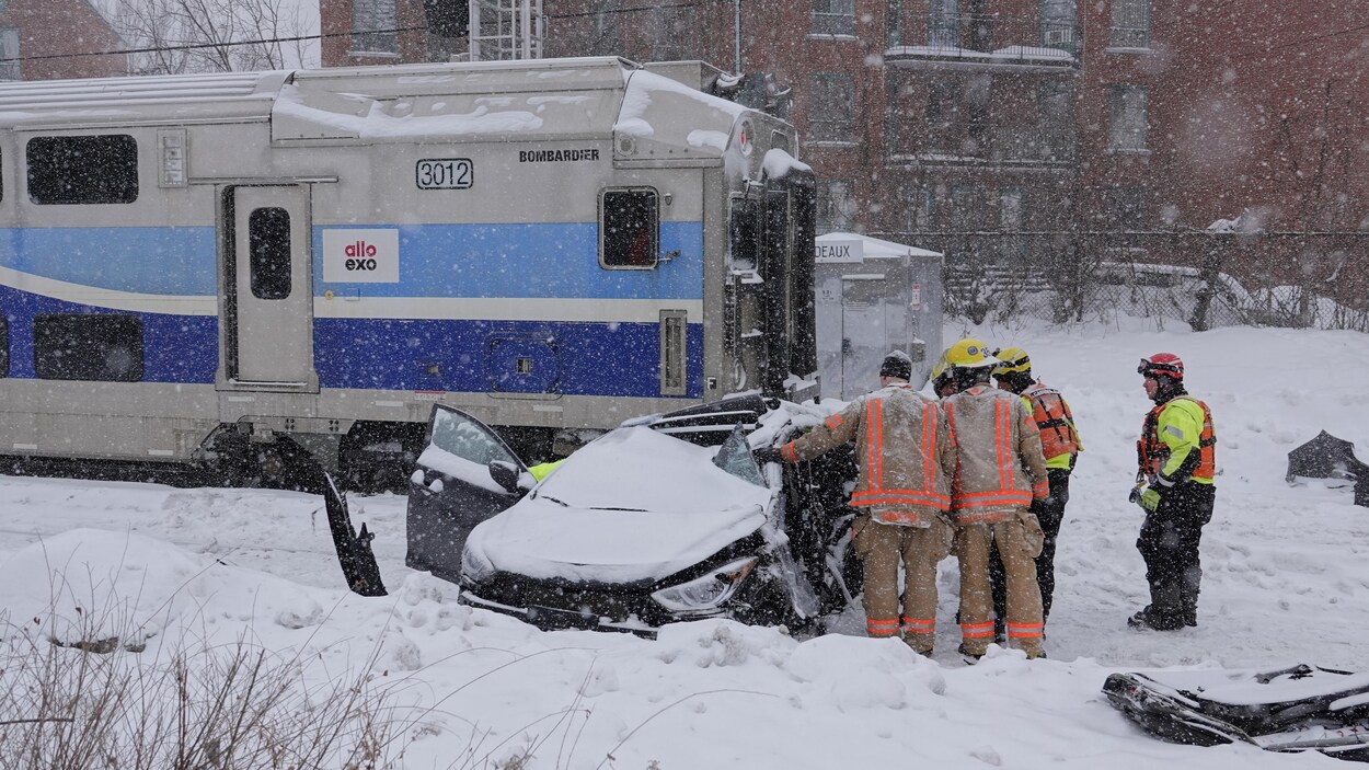 Une voiture emboutie par un train entourée de pompiers et secouristes.