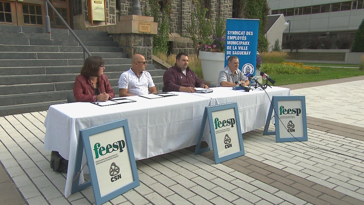 Des représentants syndicaux assis à une table de conférence de presse devant l'hôtel de ville Des représentants syndicaux assis à une table de conférence de presse devant l'hôtel de ville