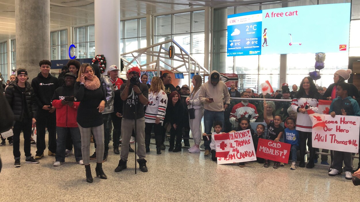 Des gens avec des pancartes et des drapeaux sont ensemble dans un aéroport.