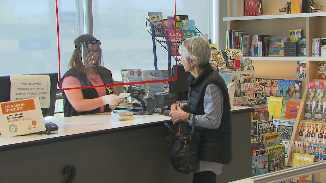 Une caissière portant une visière tend une facture à une cliente.