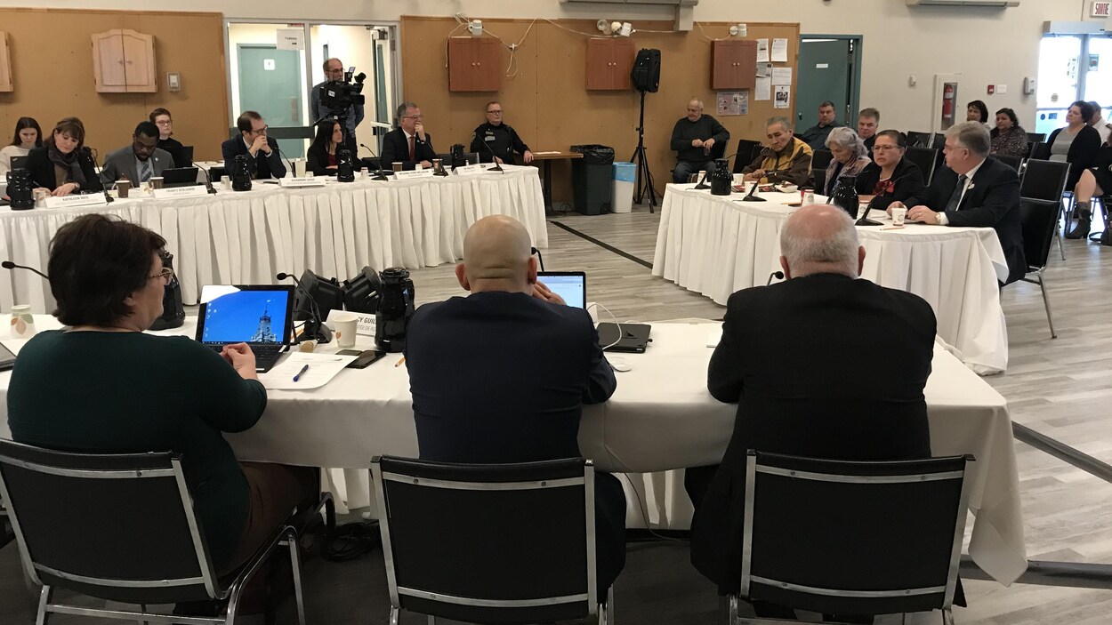 Des gens sont assis à des tables et écoutent des personnes qui sont assises à une table avec des micros.