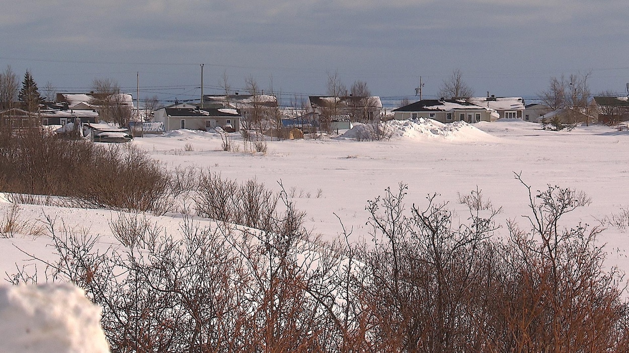 Au bout d'un champ enneigé, quelques maisons sont alignées.