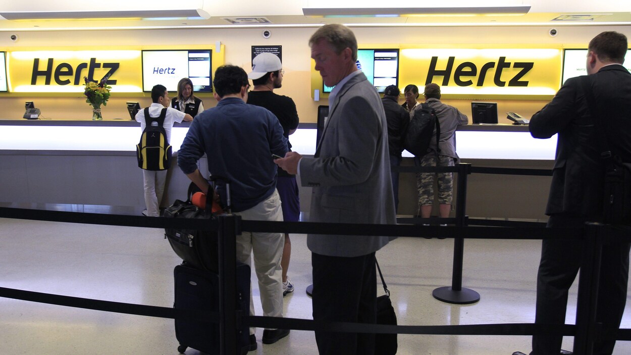 Des clients attendent en ligne pour être servis au comptoir par des employés de Hertz.
