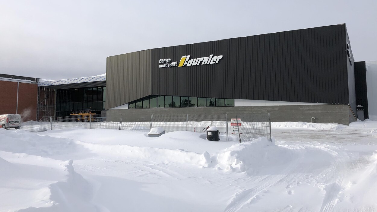 La façade du Complexe Multisport, avec devant une clôture de chantier de construction.