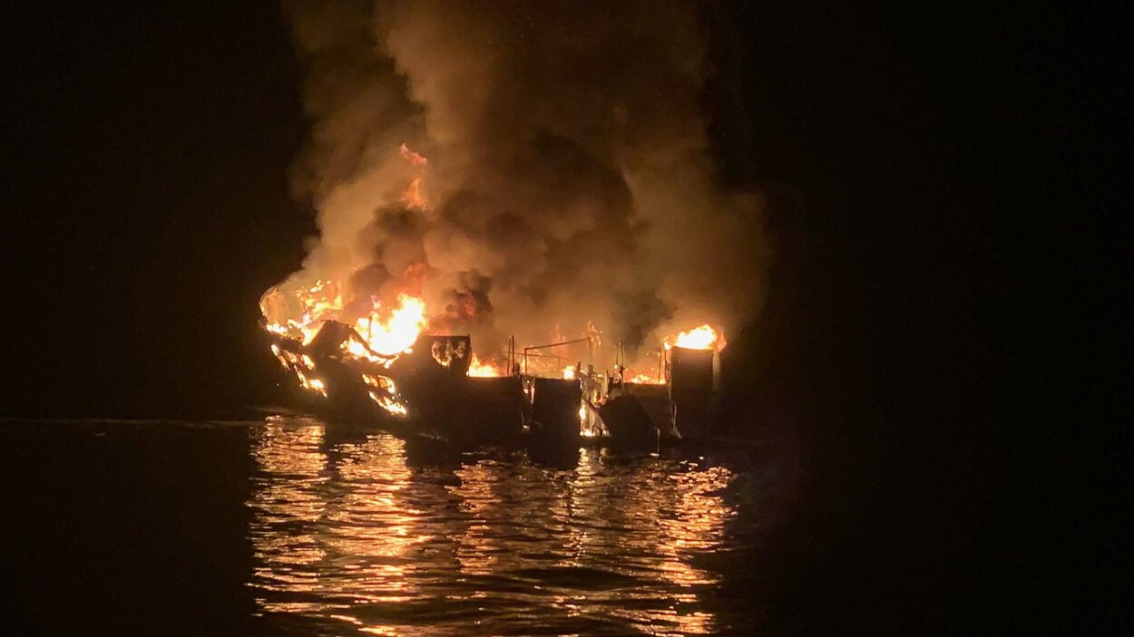Un bateau ravagé par les flammes en pleine nuit.