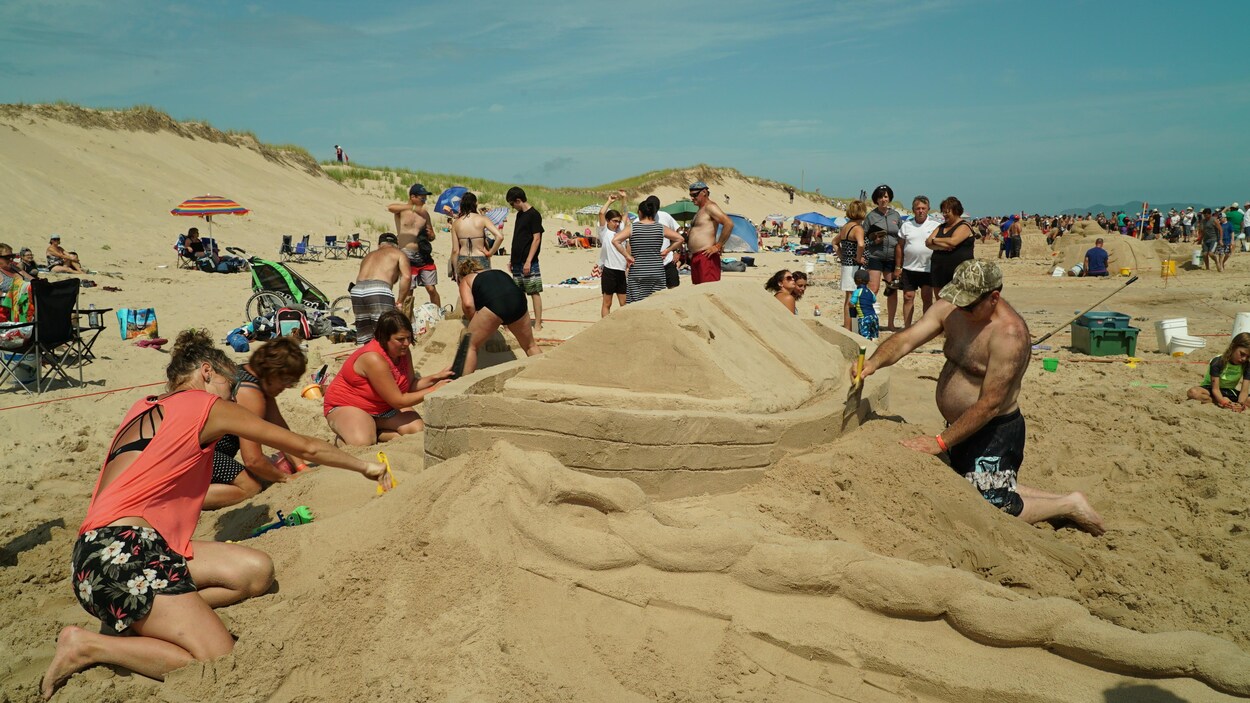 Un homme et quatre femmes sculptent un bateau dans le sable.