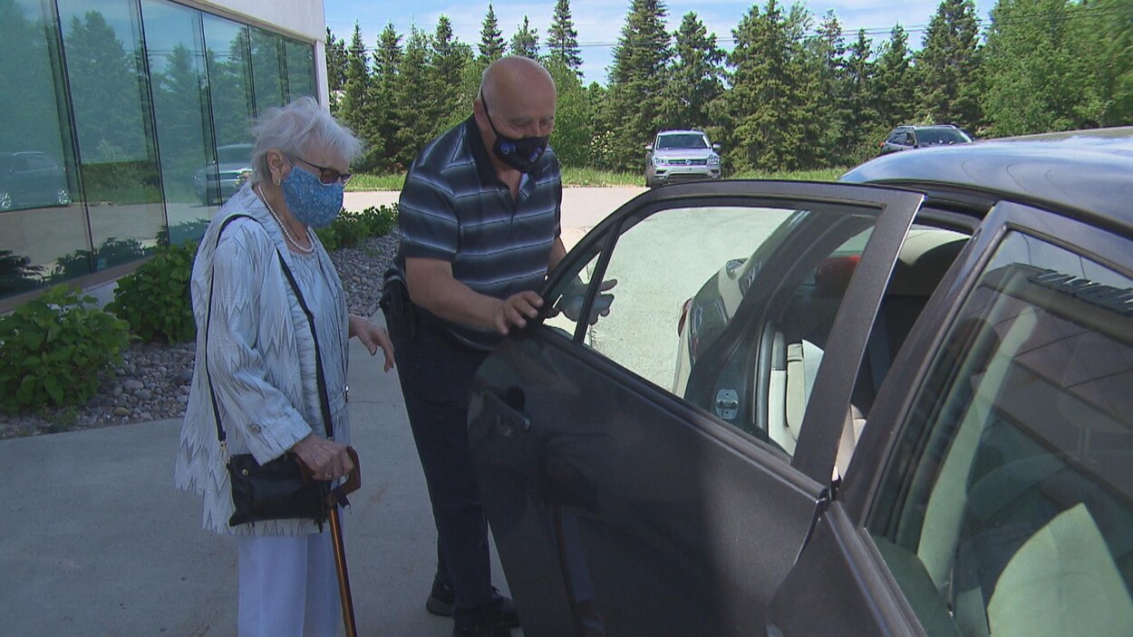 Un bénévole ouvre la portière de sa voiture à une dame âgée.