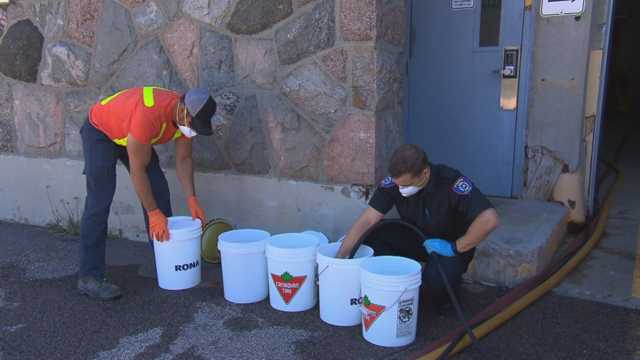Un pompier et un travailleur remplissent des chaudières d'eau potable.
