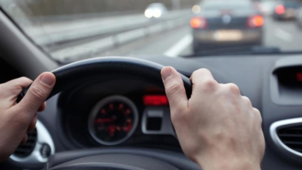 Des mains sur un volant dans une voiture.