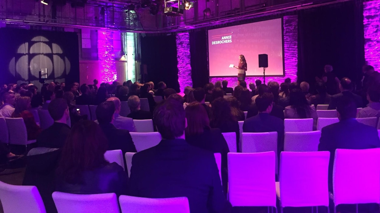 Une salle comble écoute Annie Desrochers parler sur une estrade.