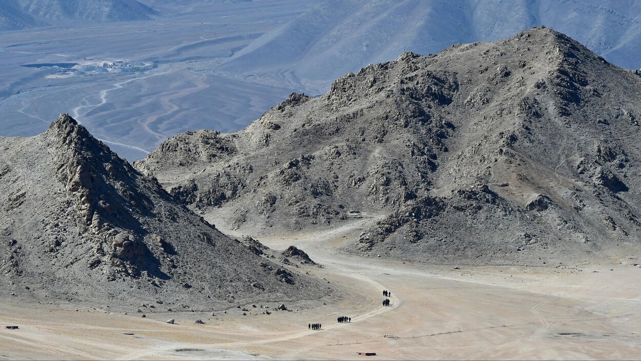Au loin, une trentaine de soldats marchent en quatre pelotons à travers des montagnes désertiques.