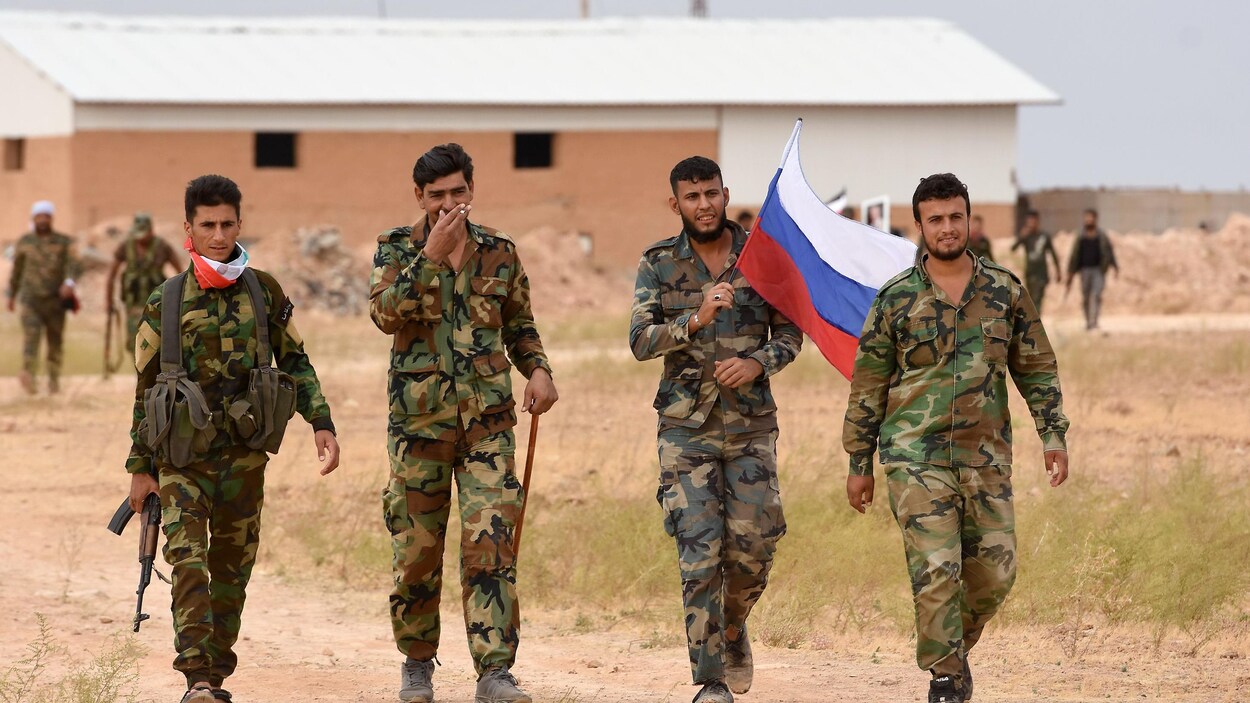 Des soldats syriens marchent et l'un d'eux tient en main un drapeau russe.