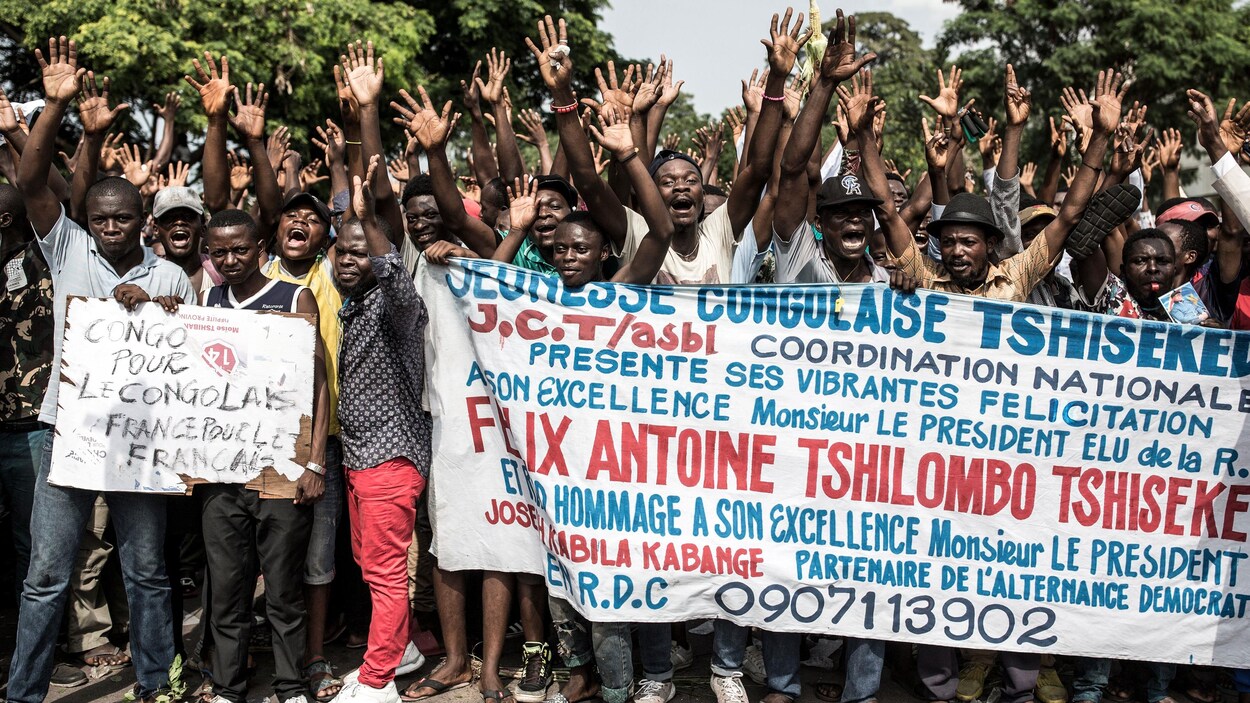 Des Congolais lèvent les bras en l'air tout en tenant une banderole dans une rue de Kinshasa.