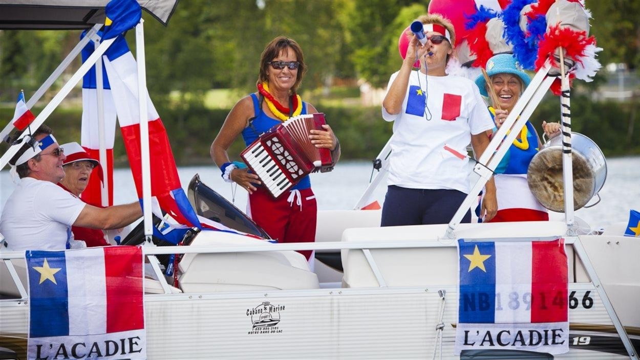 Sur un bateau, plusieurs personnes font la fête aux habillés aux couleurs de l'Acadie.