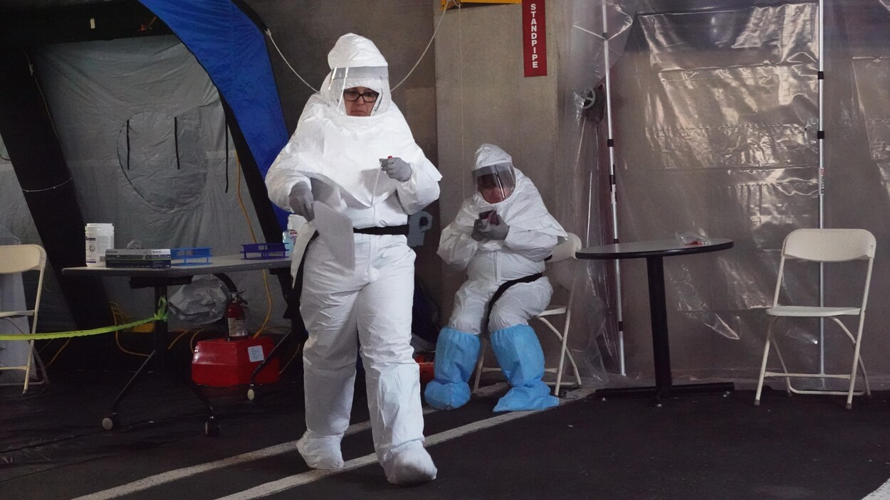 Deux personnes portant des combinaisons blanches près d'une tente.