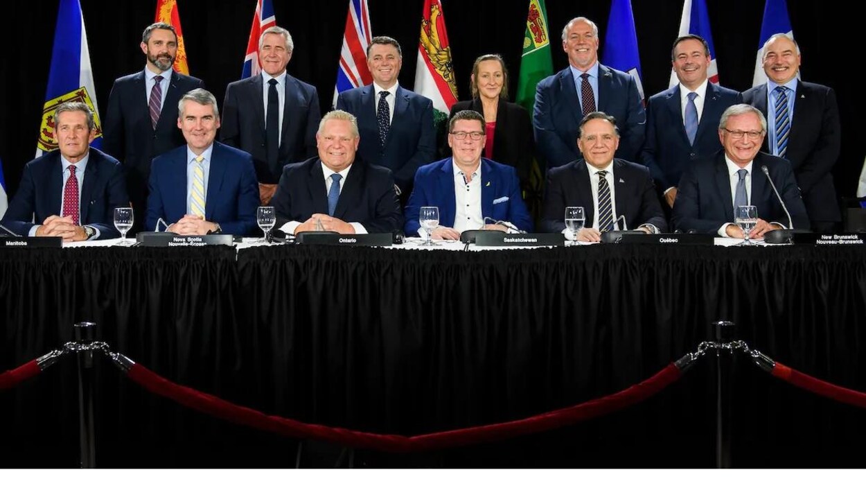 Photo de groupe des 13 premiers ministres des provinces et territoires canadiens dont six à l'avant assis derrière une table et sept debout derrière eux.