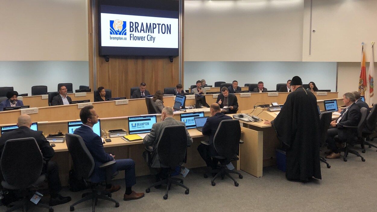 Séance au conseil municipal où un membre d'une délégation chrétienne s'exprime devant des conseillers municipaux.