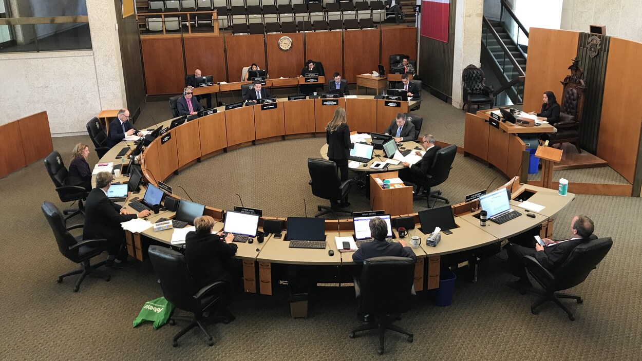 Des conseillers municipaux assis à deux mètres de distance les uns des autres, autour d'une table ronde.